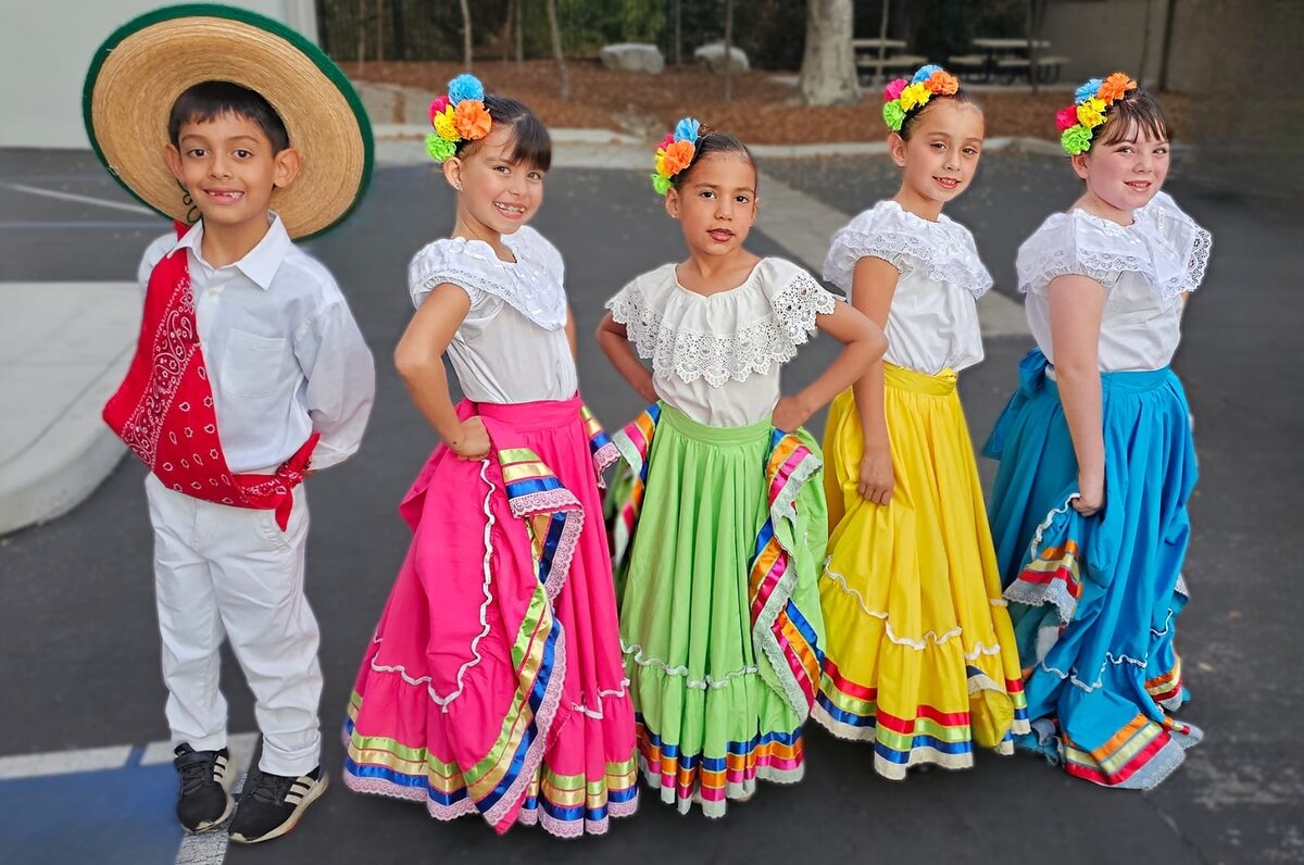 Folklórico dancers in colorful ribboned skirts posing together outdoors after a performance