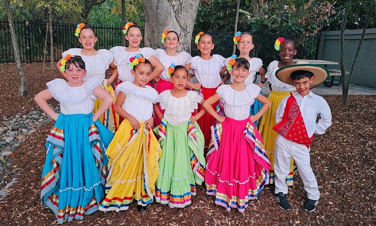 A group of Folklórico dancers and a young dancer in a sombrero and red bandana posing together